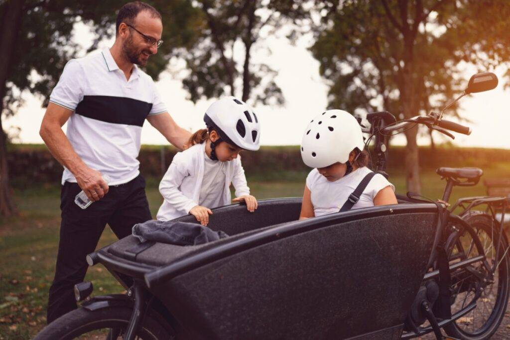 A father and two children getting on a cargo bike outdoors